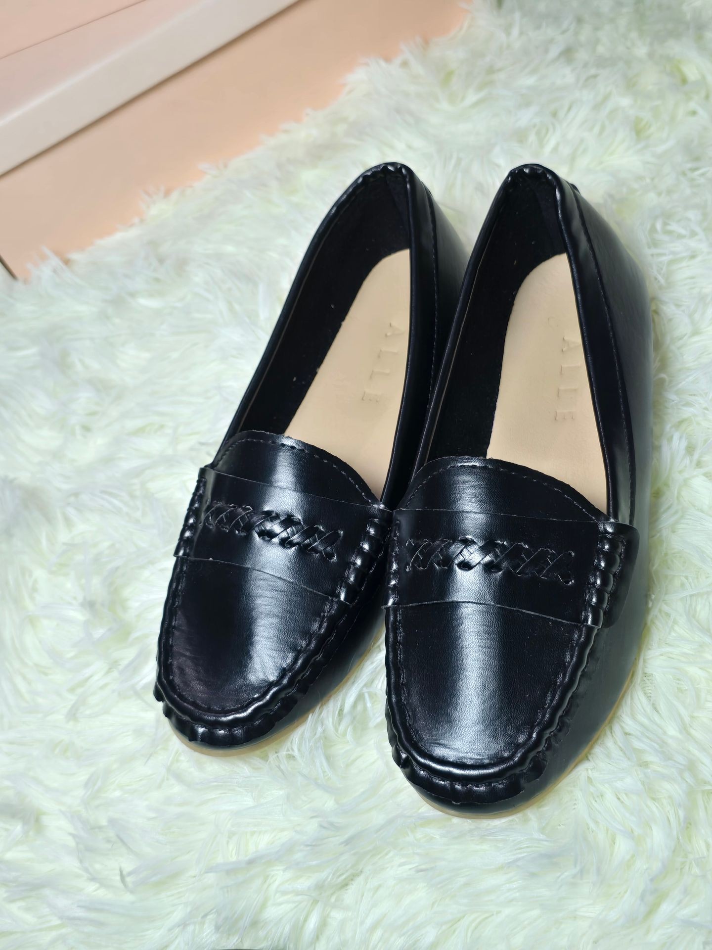 Pair of black leather loafers on a light green fluffy carpet.