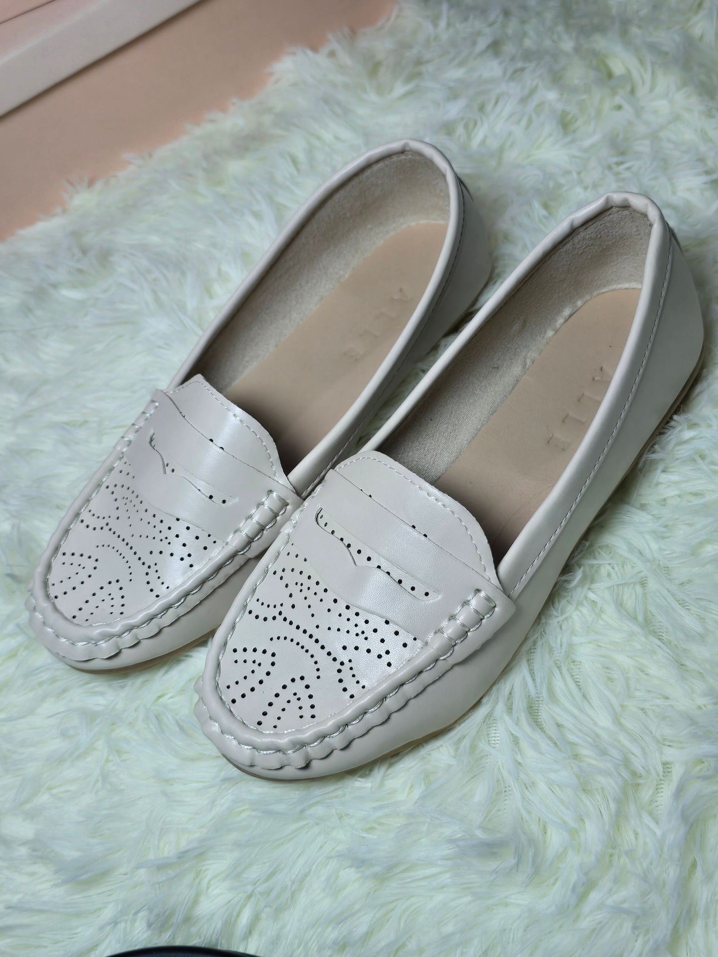 Pair of white leather loafers with intricate perforated design, placed on a fluffy white rug.