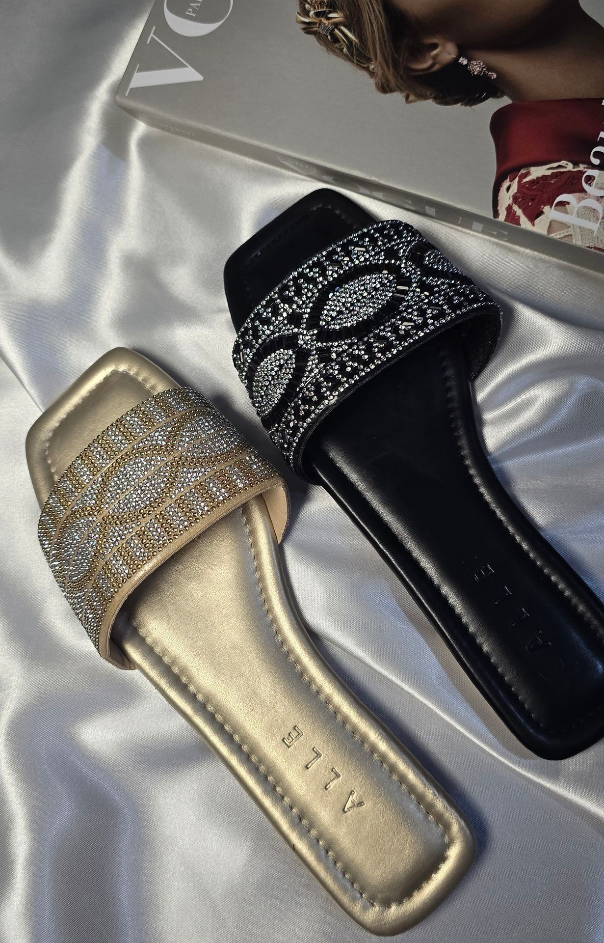 Gold and black embellished slides placed on a satin fabric next to a fashion magazine.