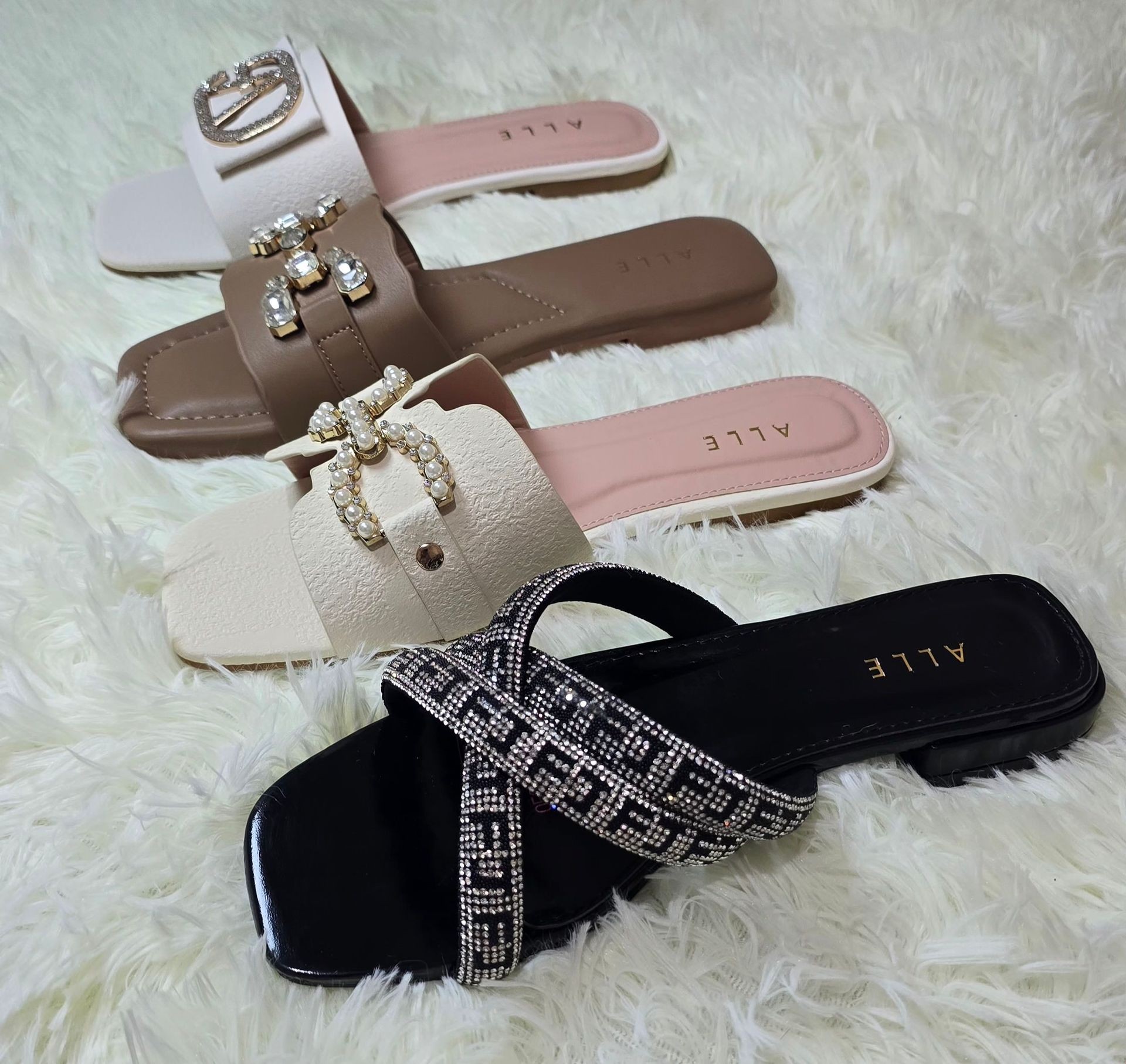 Three pairs of stylish sandals with embellishments displayed on a soft, white shag rug.