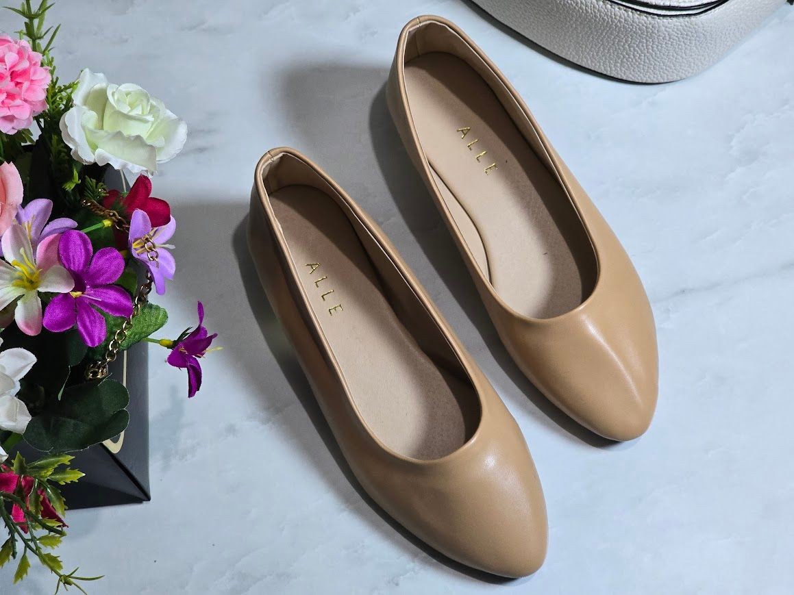 A pair of beige flat shoes on a marble surface next to a bouquet of colorful flowers.