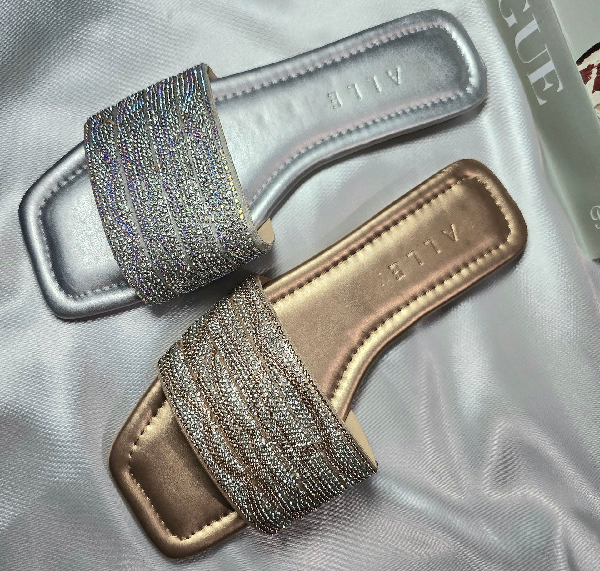 Pair of silver and gold sandals with beaded straps, laid on a satin surface.