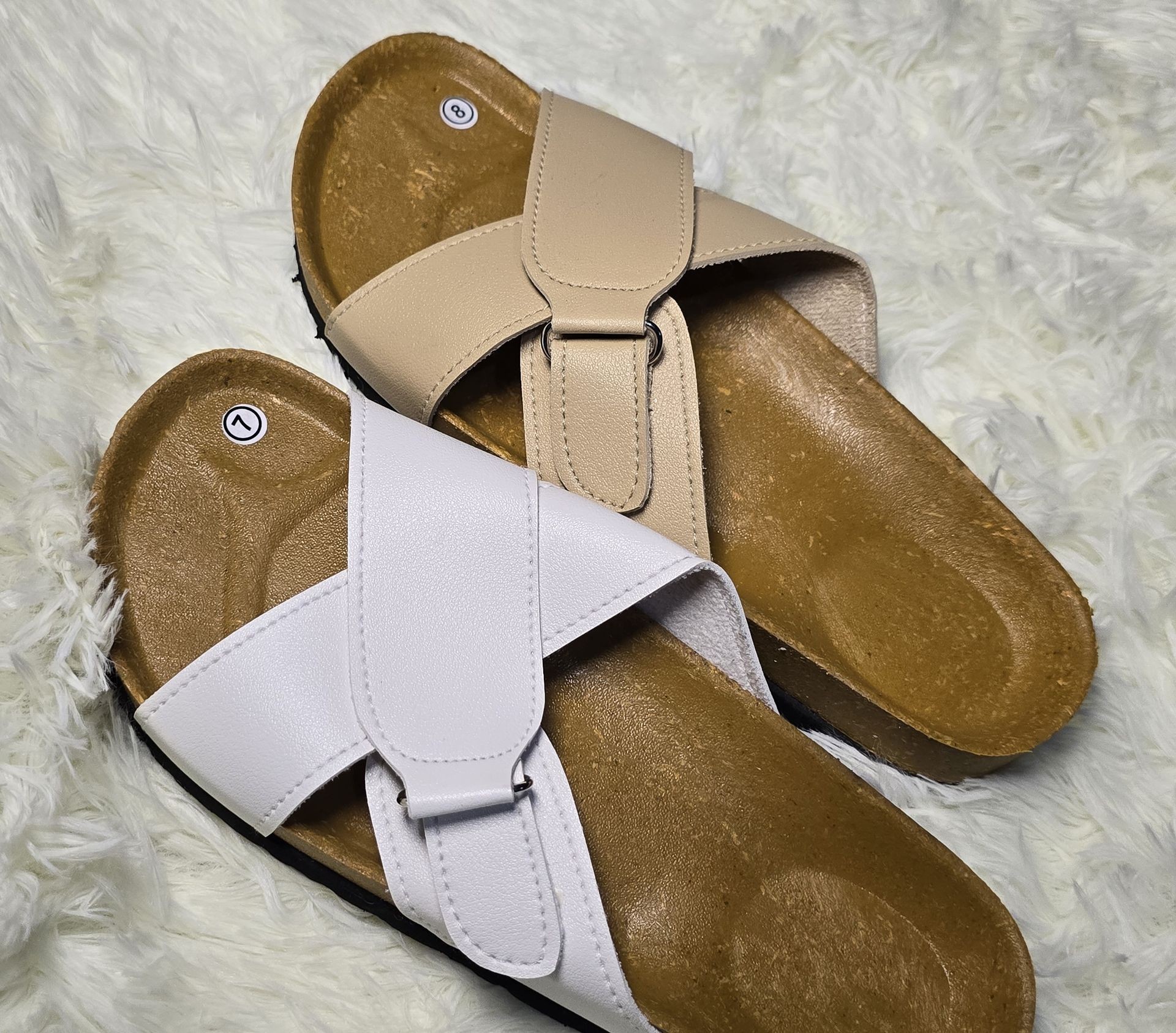 Pair of beige and white open-toe sandals with brown soles on a fluffy white surface.