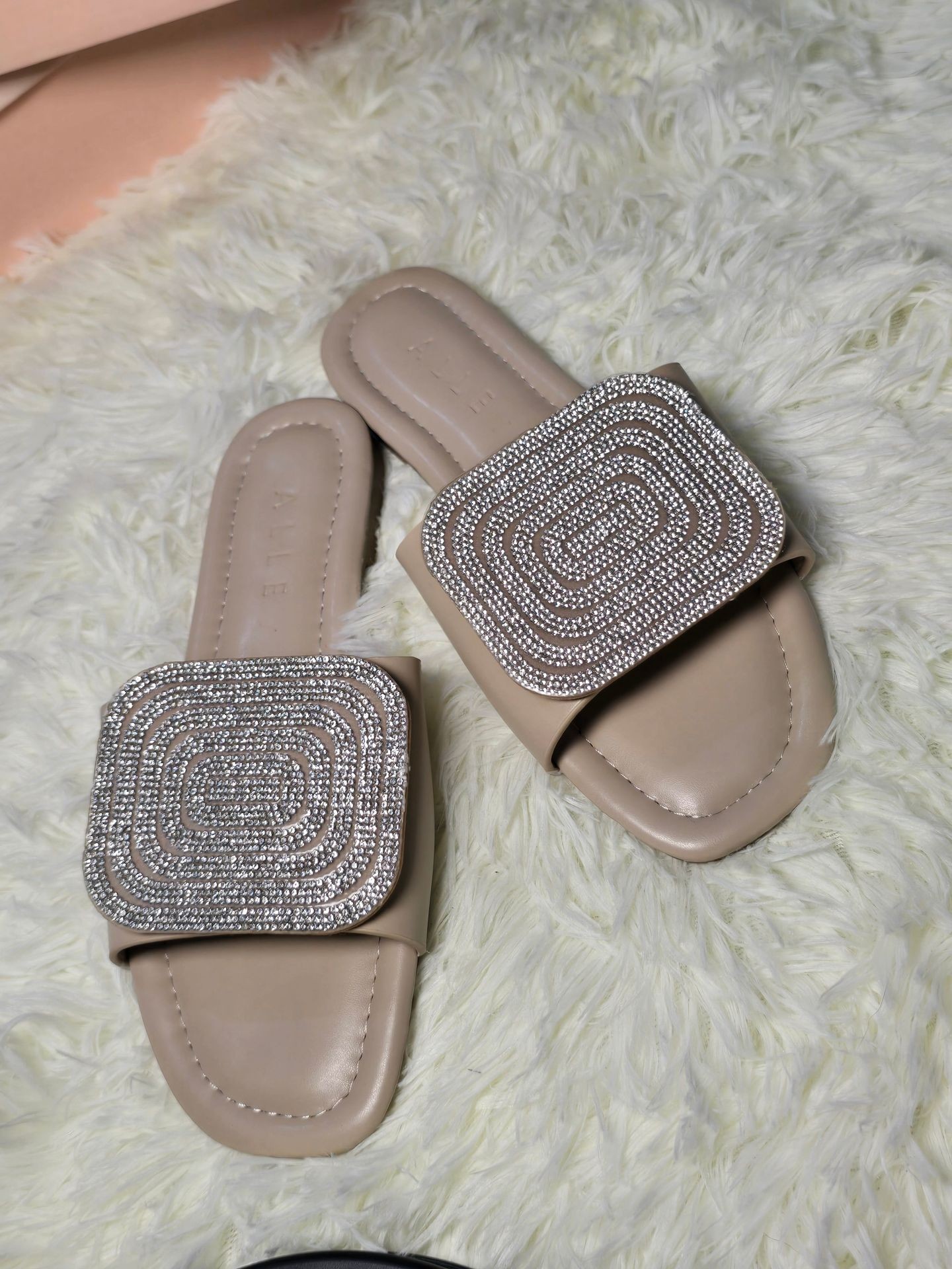 Pair of beige sandals with intricately beaded decorative straps, placed on a fluffy white rug.