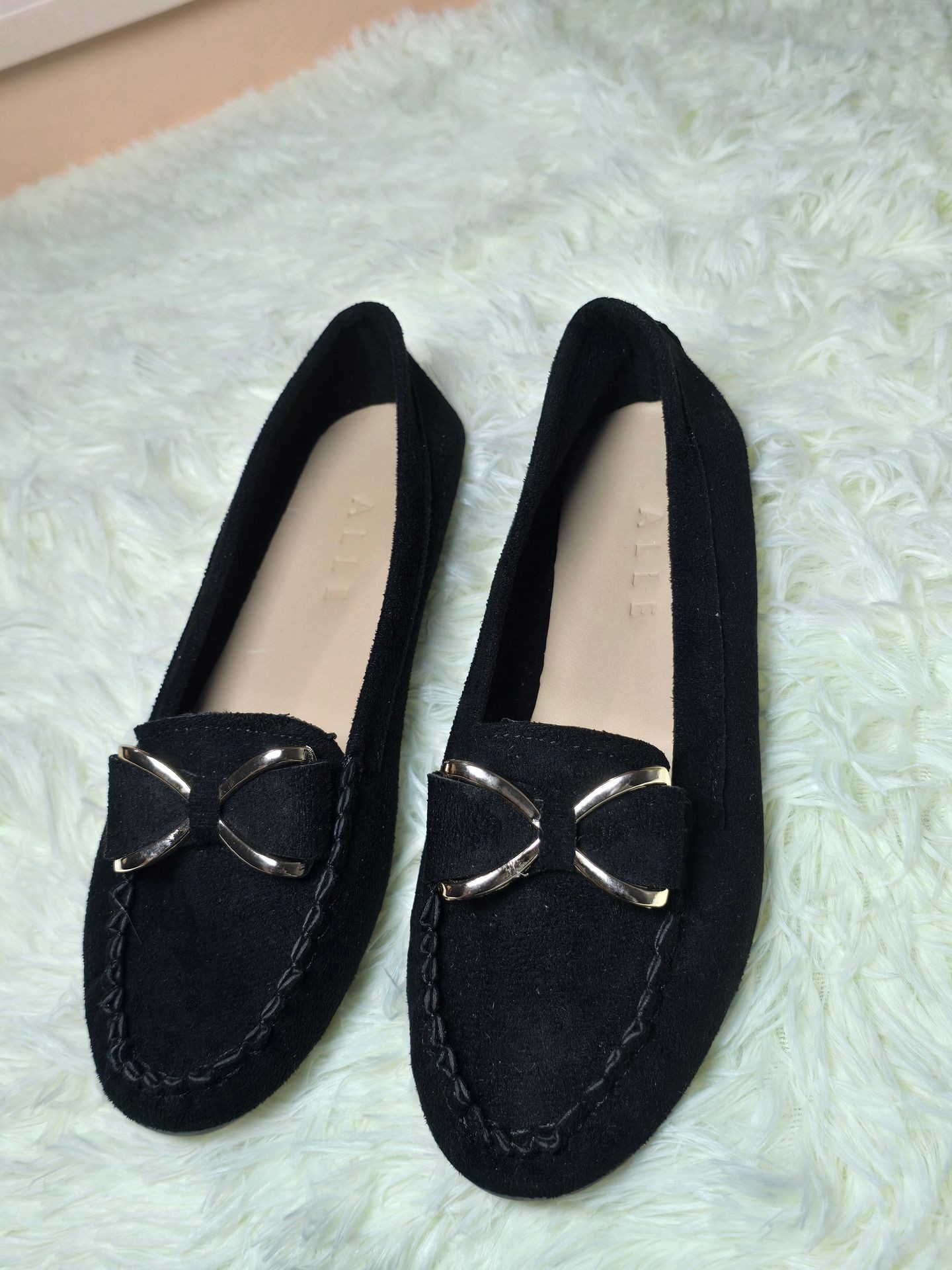 Pair of black loafers with metallic bow accents on a fluffy light green rug.