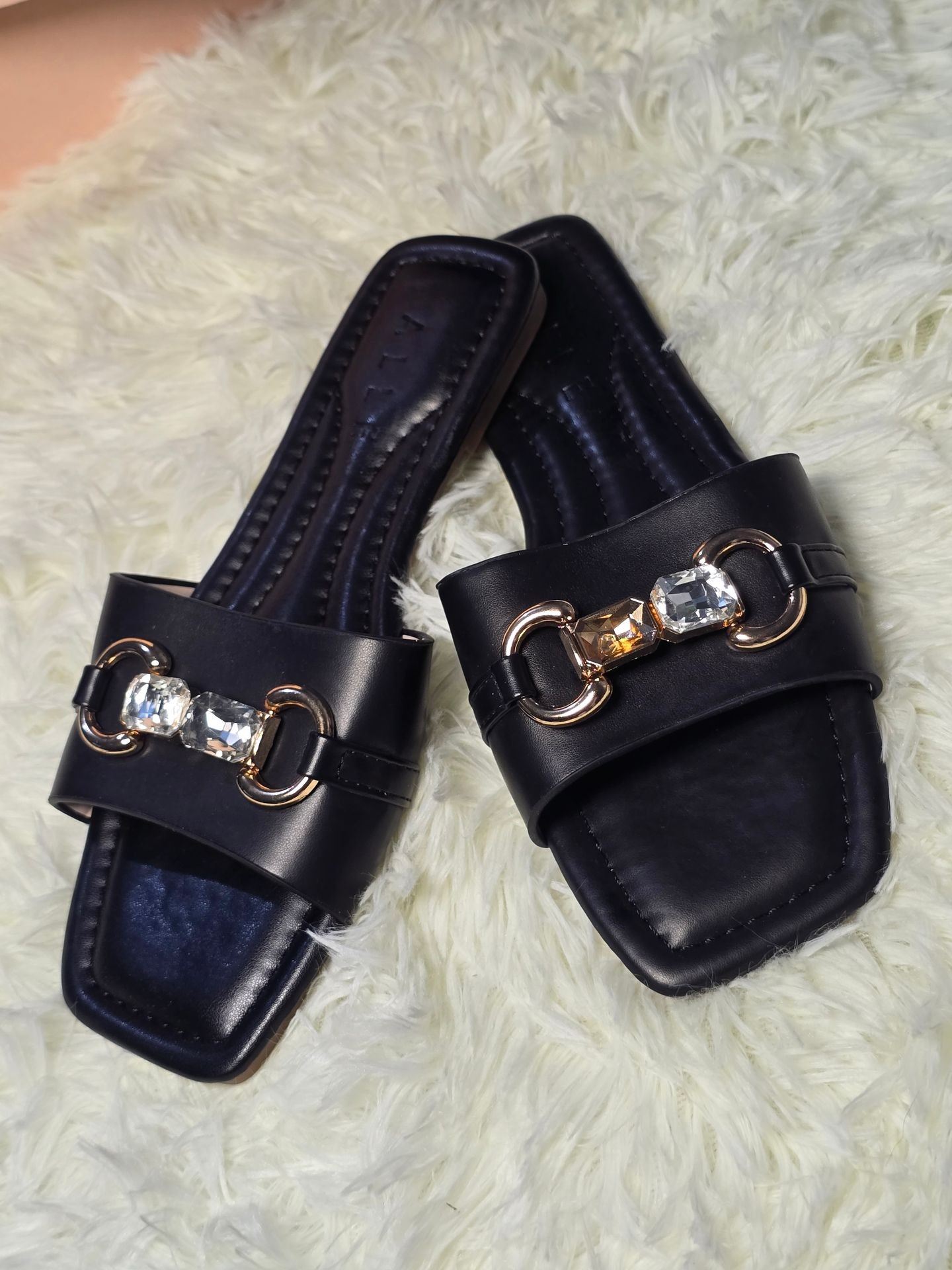 Pair of black sandals with gold and crystal decorations on a white fluffy surface.