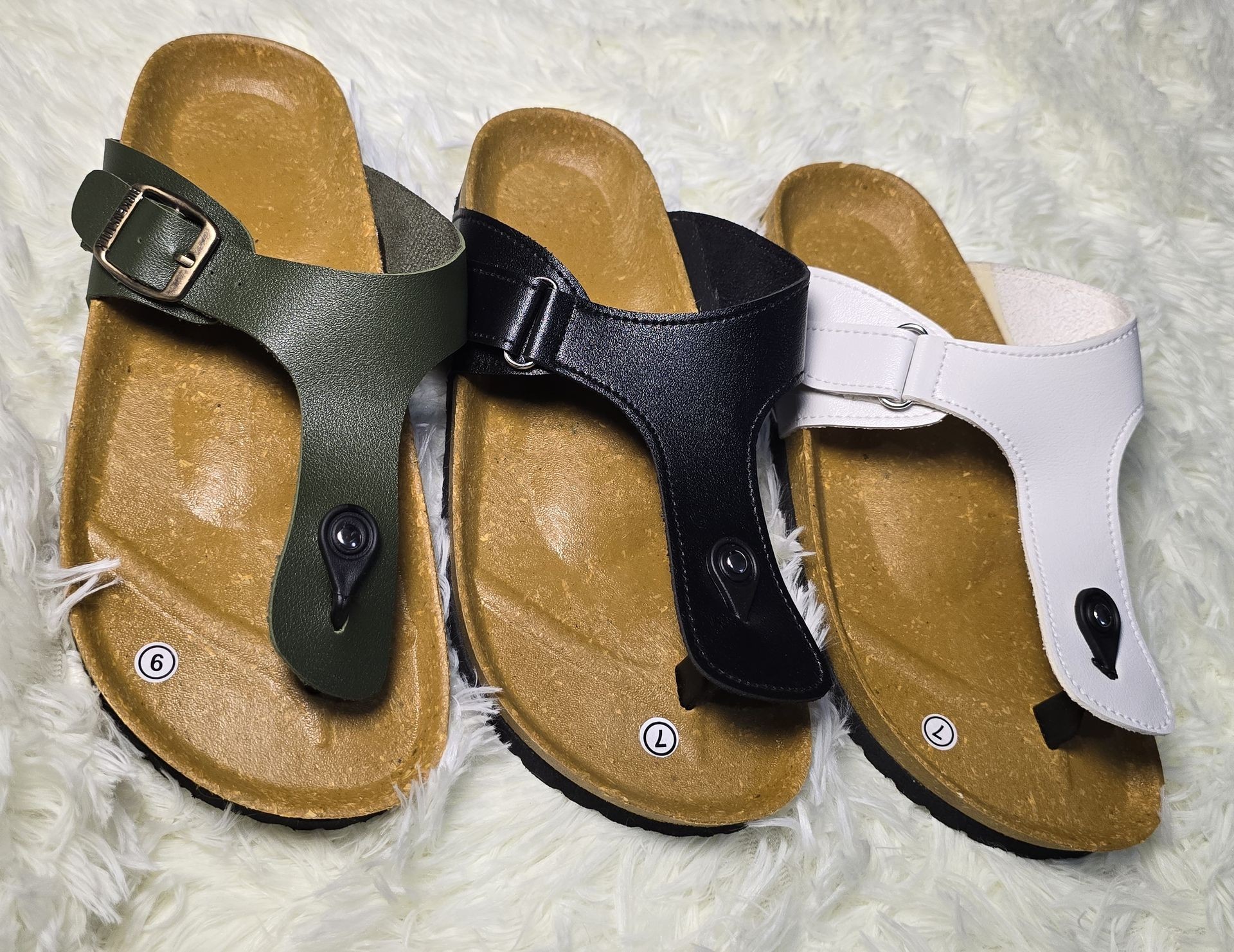 Three pairs of leather sandals in green, black, and white colors on a fluffy white surface.