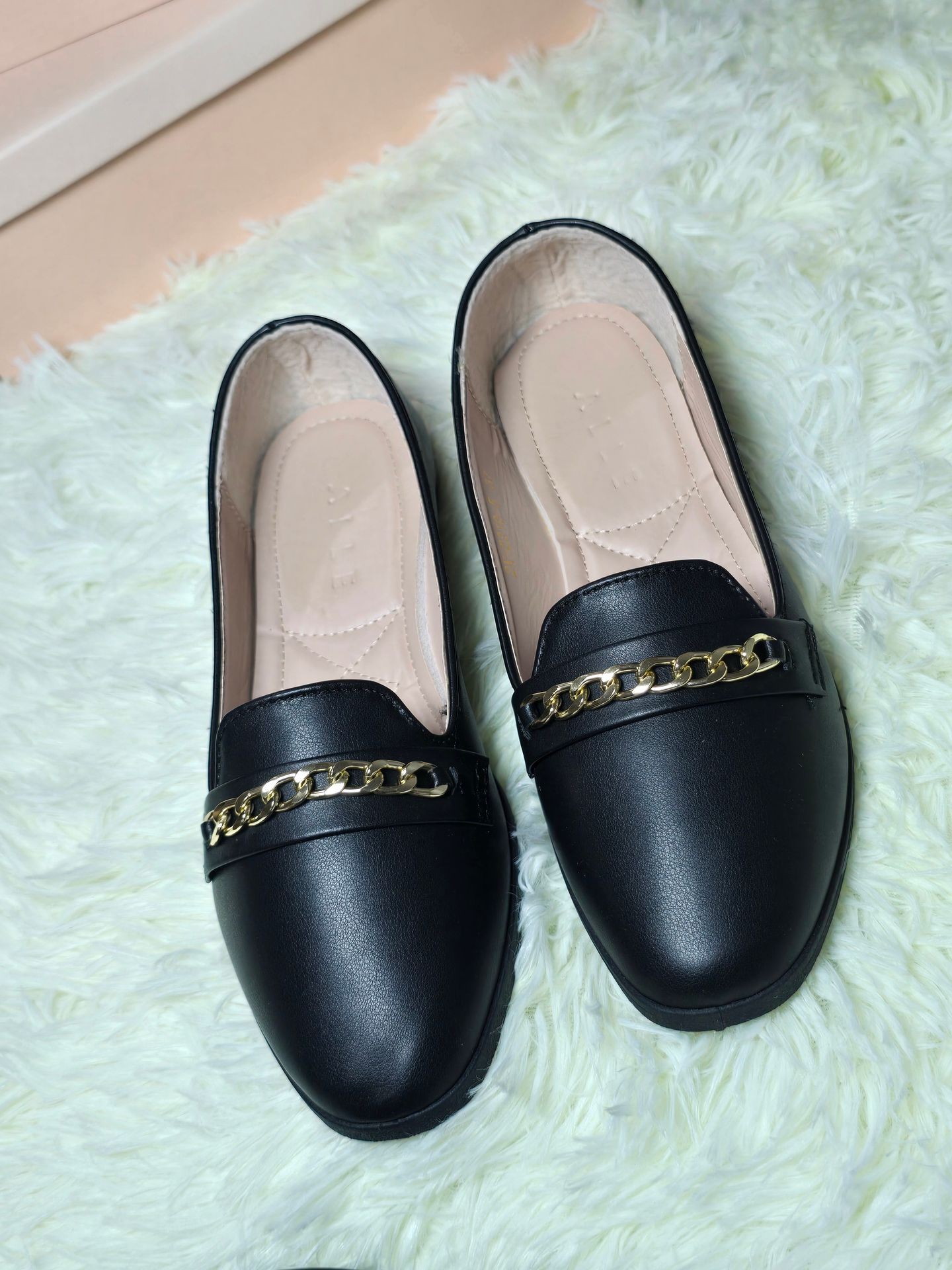 Pair of black loafers with gold chain detail on a light green fluffy rug.